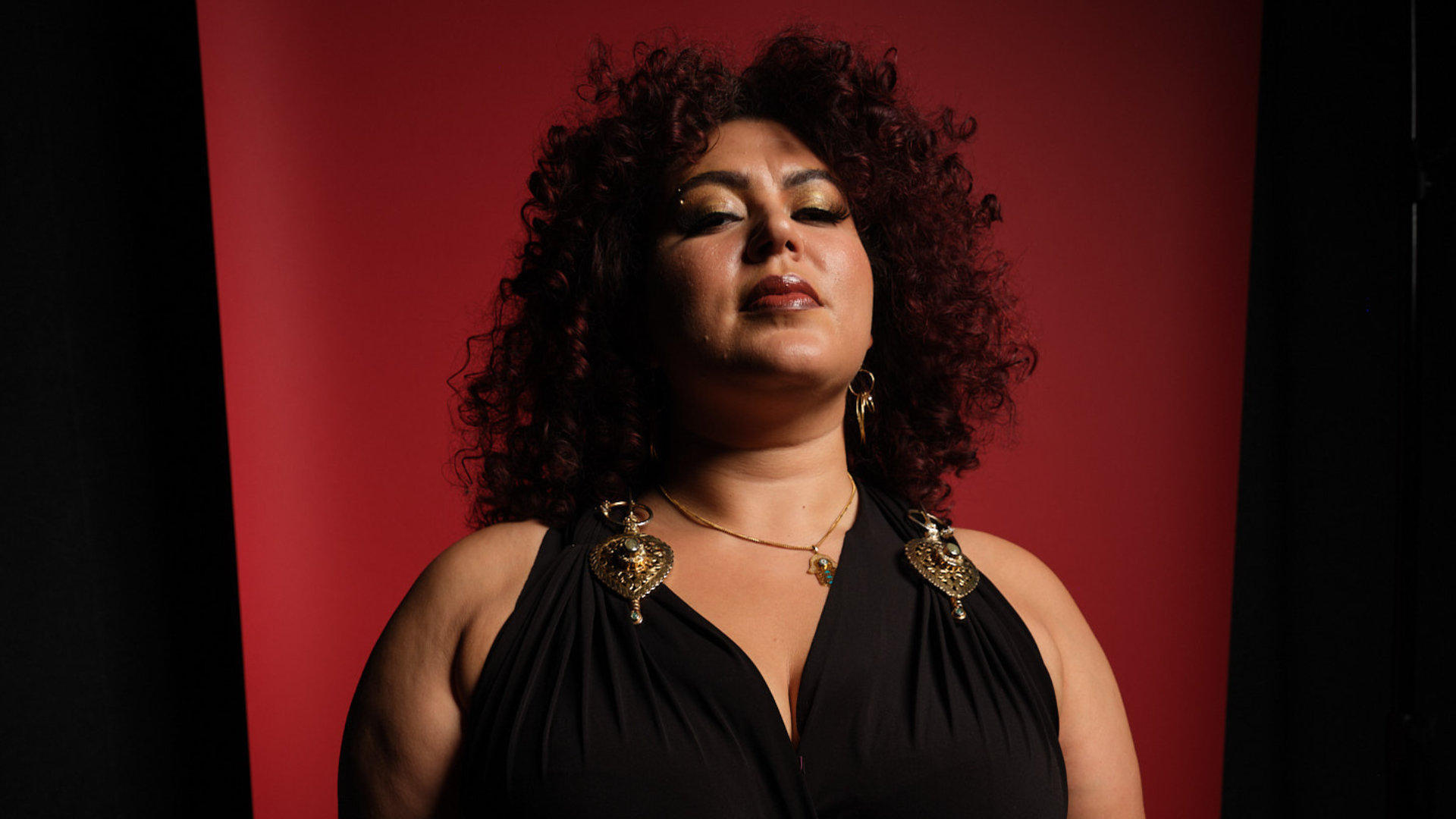 image of performer, black and red background, north african woman with curly hair to shoulders wearing a black top