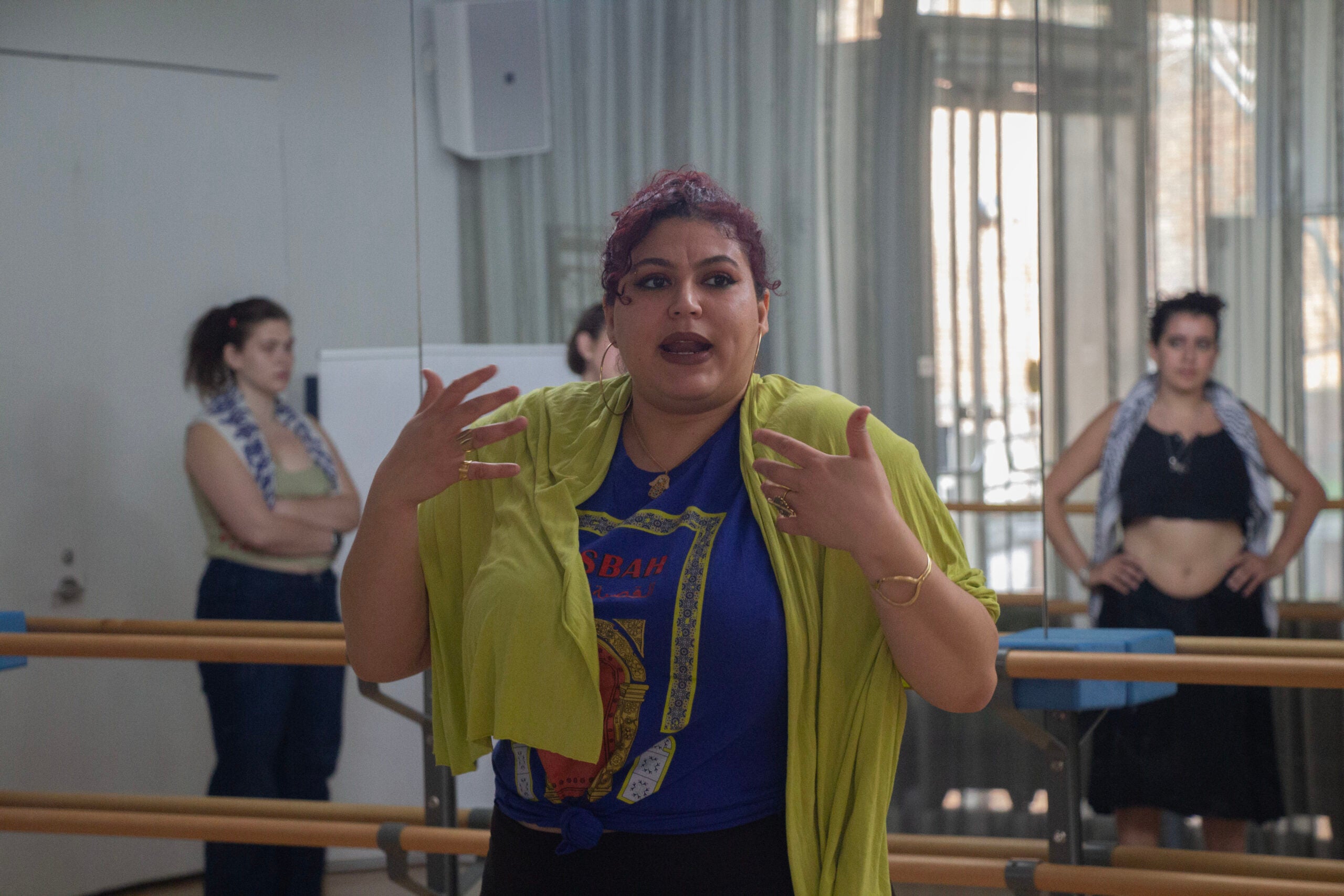 Warda, in a blue shirt, hoops, bold lipstick and lime green shawl over her shoulders, is addressing a dance studio full of eager participants.