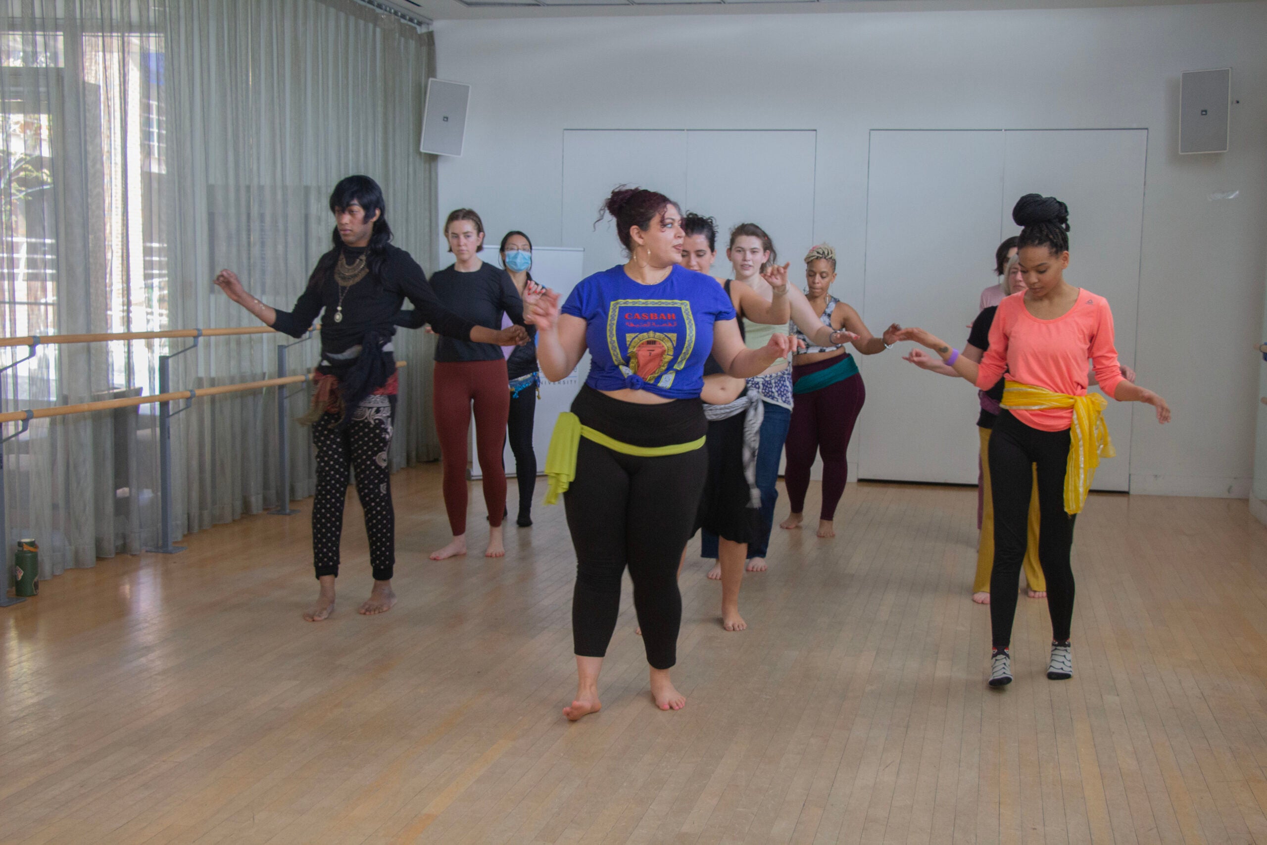 The dancers of various ethnicities and genders are in formation behind Warda, following her lead and instructions.