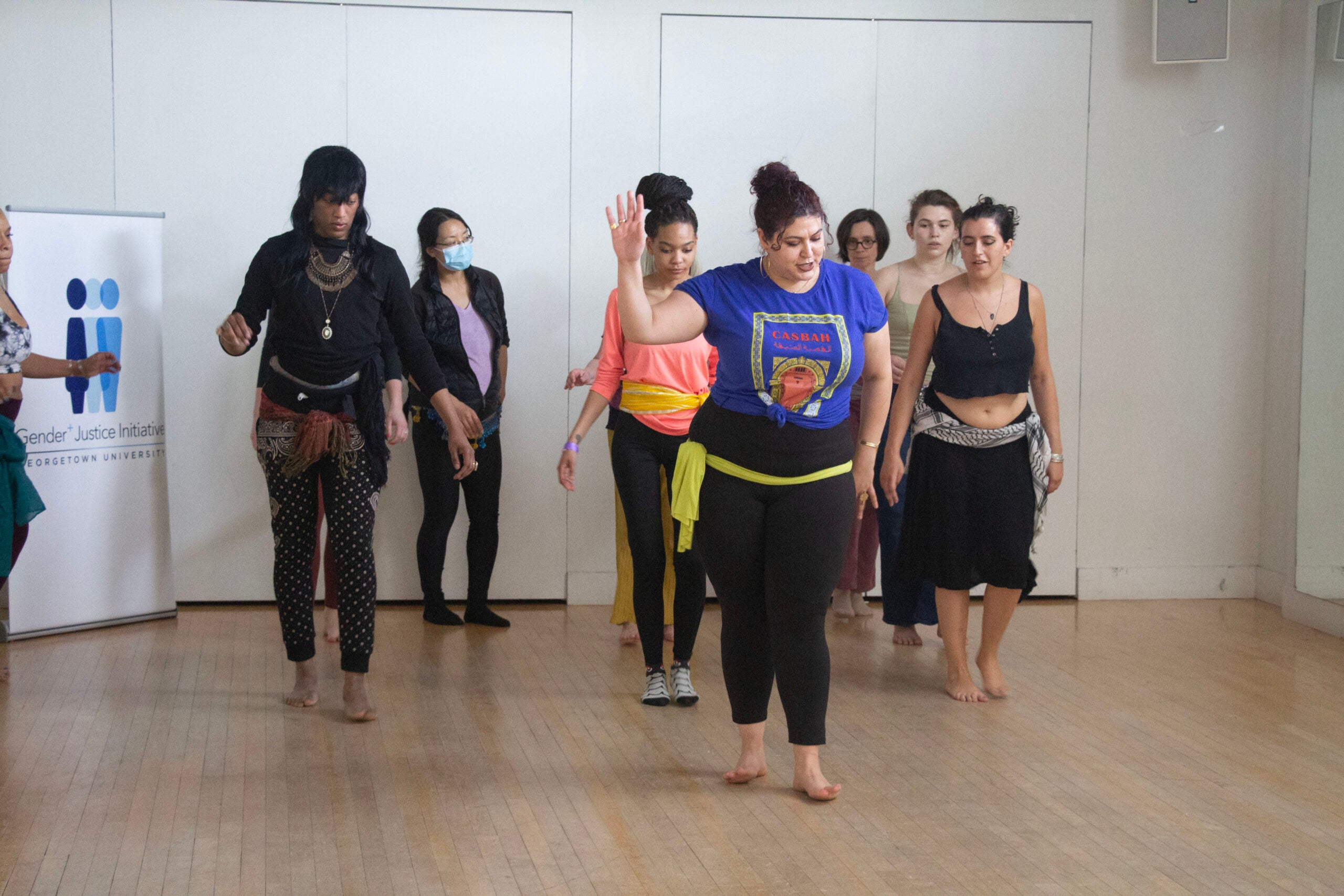 The dancers of various ethnicities and genders are in formation behind Warda, following her lead and instructions.