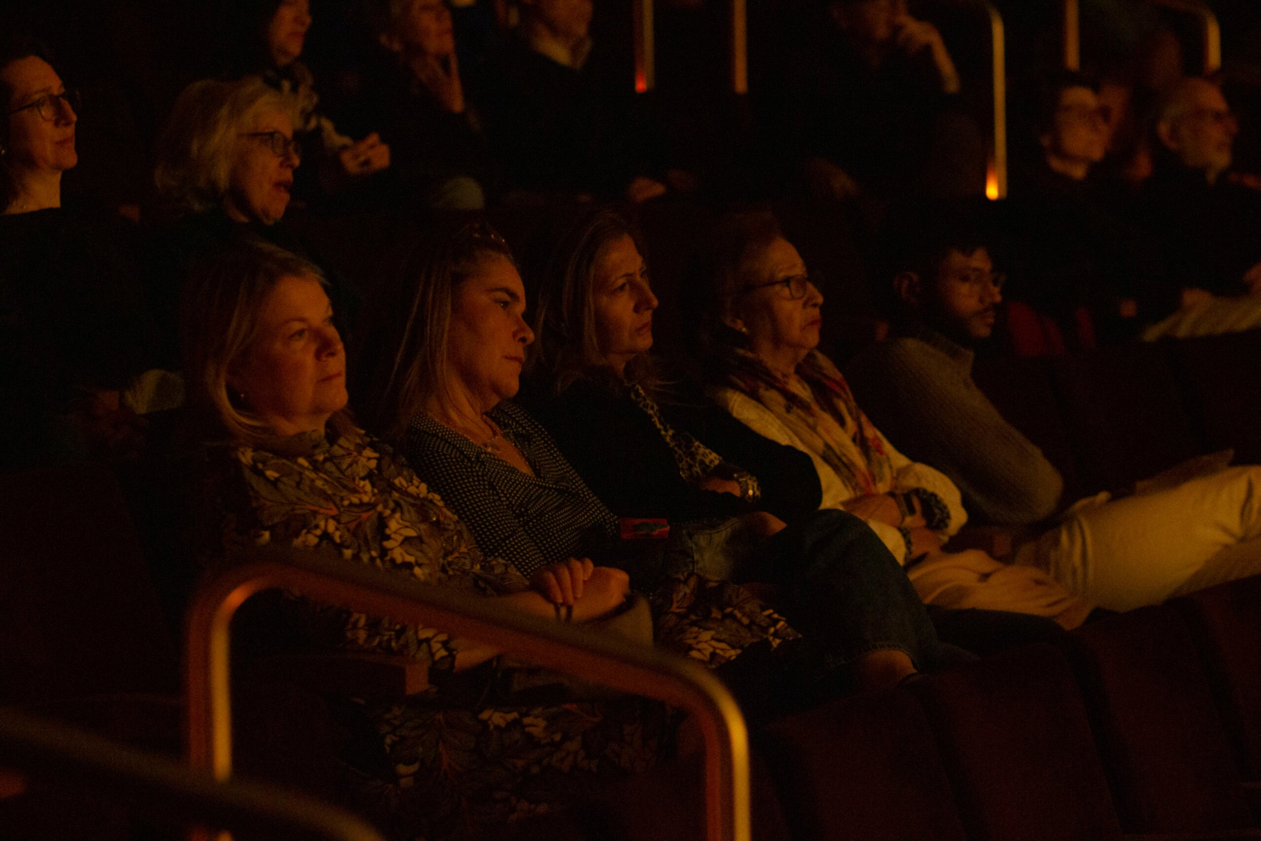Four women are seated together in a dark auditorium. They are watching the film.