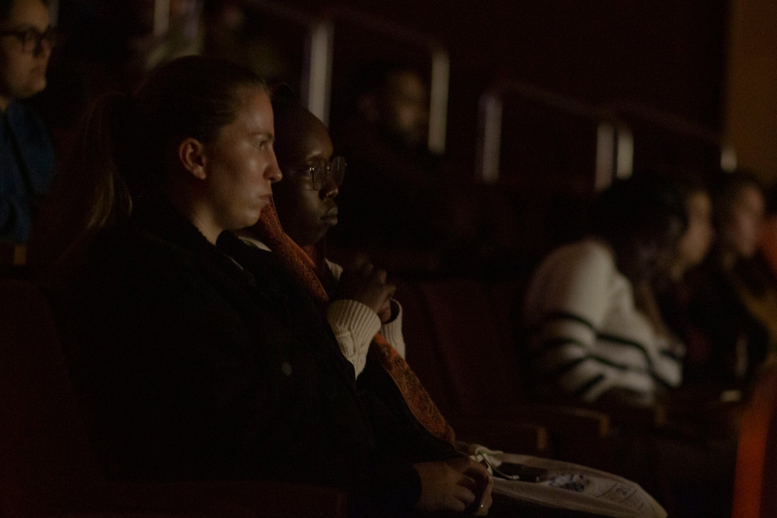 Two women are seated together in a dark auditorium. They are watching the film.