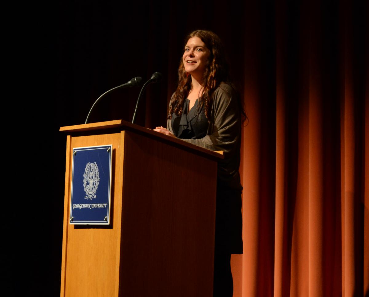 A woman with long brunette hair standing behind a Georgetown University podium, talking.