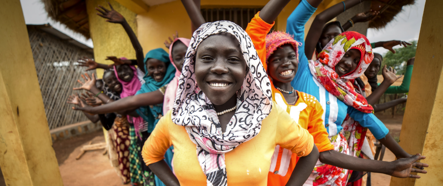 A woman with a head scarf smiling, surrounfed by other women in scarves on each side of her.