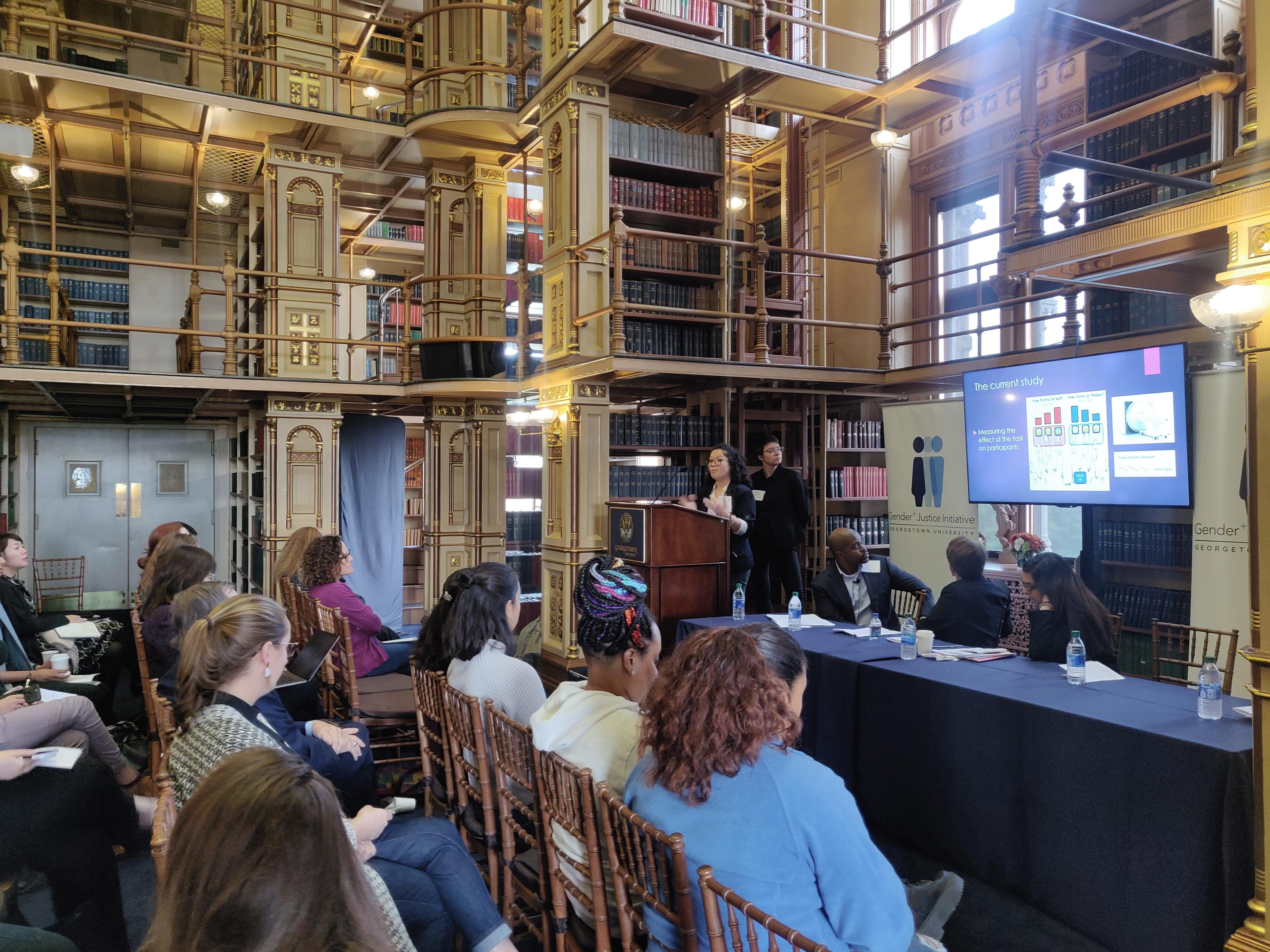A seated audience in a large library watching a lecture presentation.