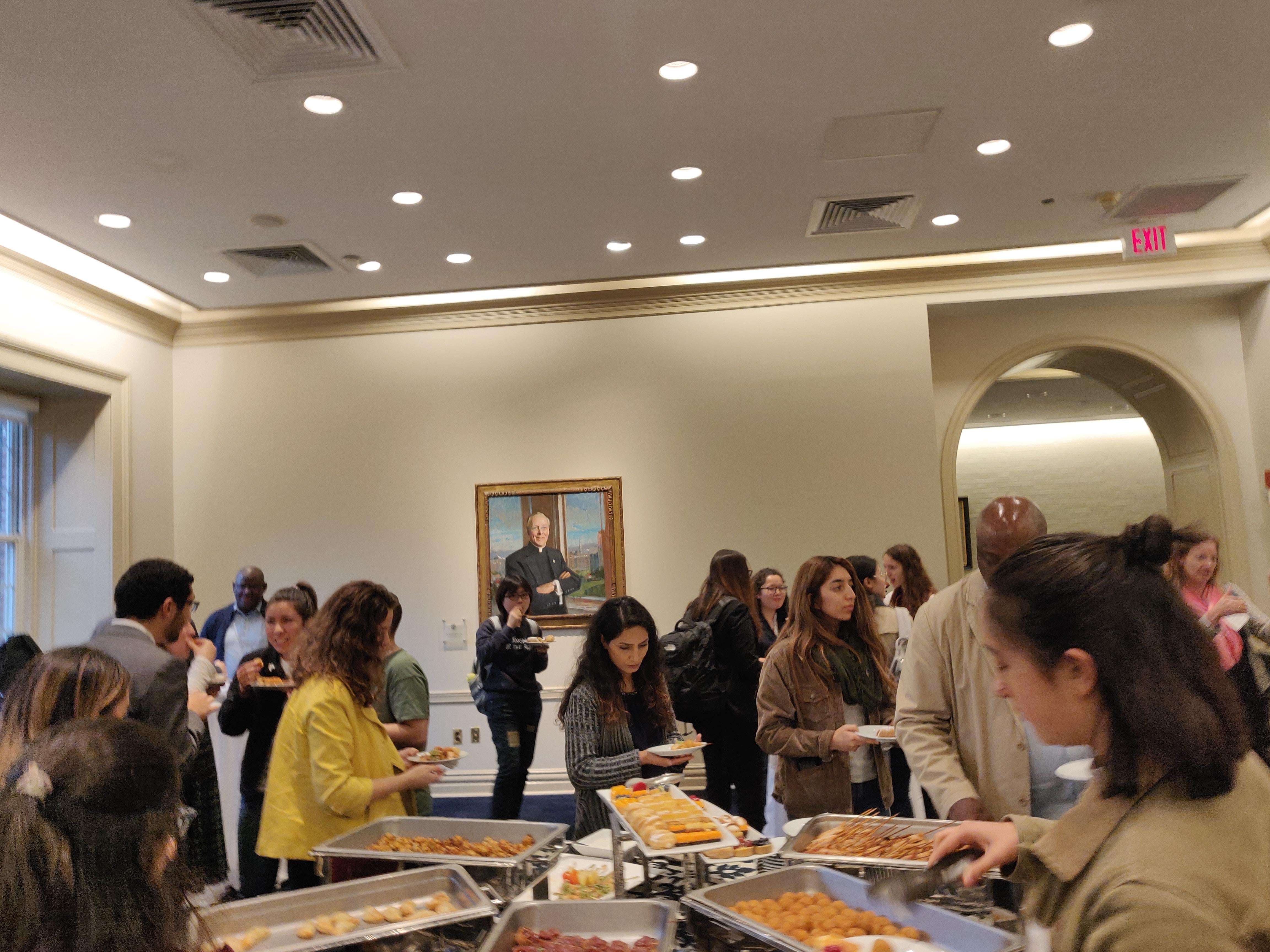 People lined up around a table of food, adding food to their plates.