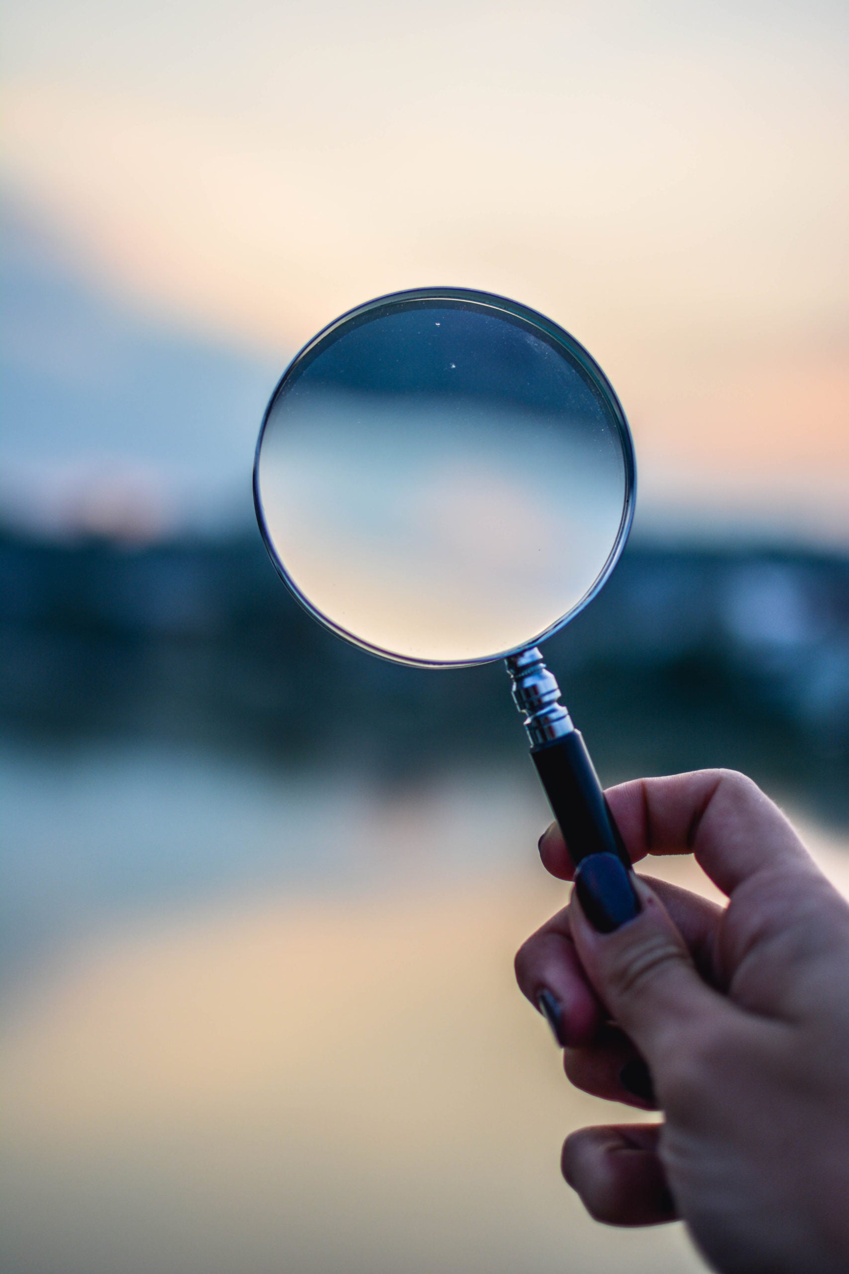 A hand holding up a magnifying glass to the sky's horizon.