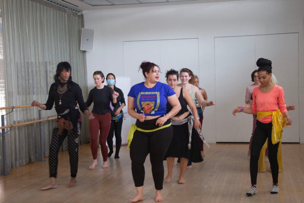 The dancers of various ethnicities and genders are in formation behind Warda, following her lead and instructions.