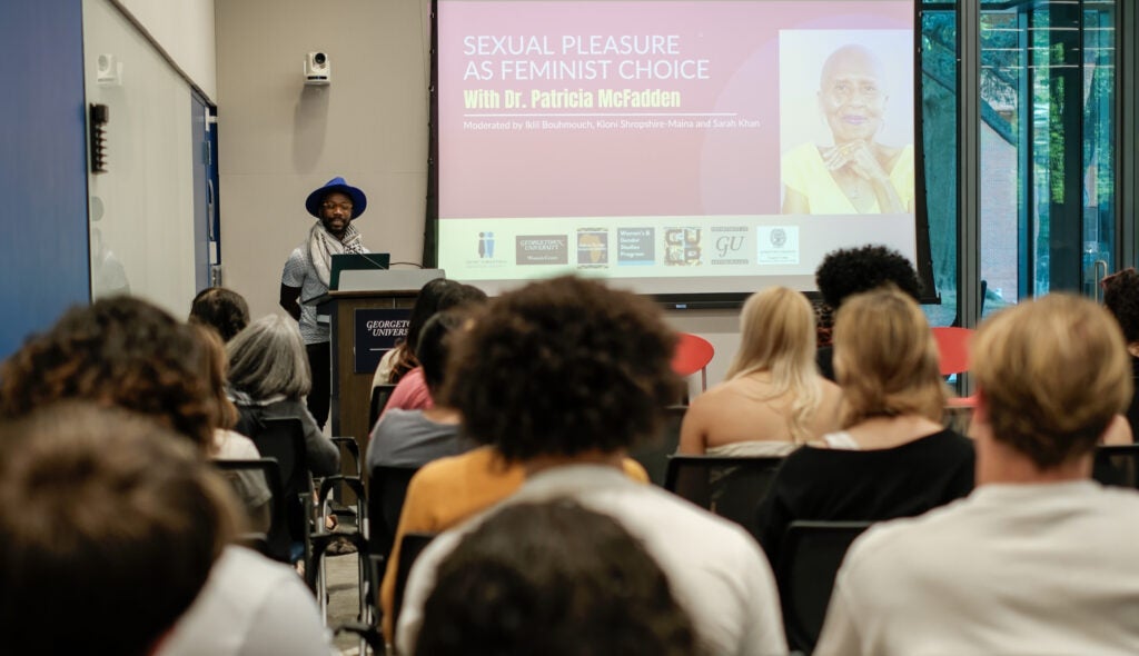 Dr. Kwame Edwin Otu, a black man in a purple hat and keffiyeh, introduces Dr. McFadden.