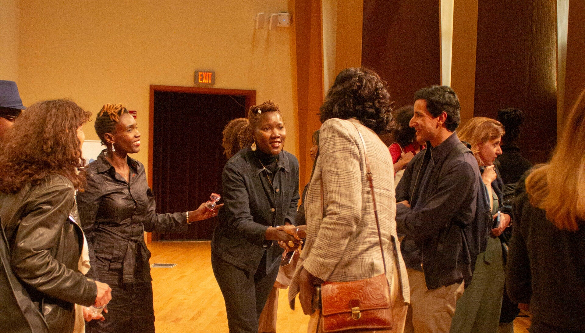 A group of people standing in a circle, chatting. Two women in the middle shake hands.
