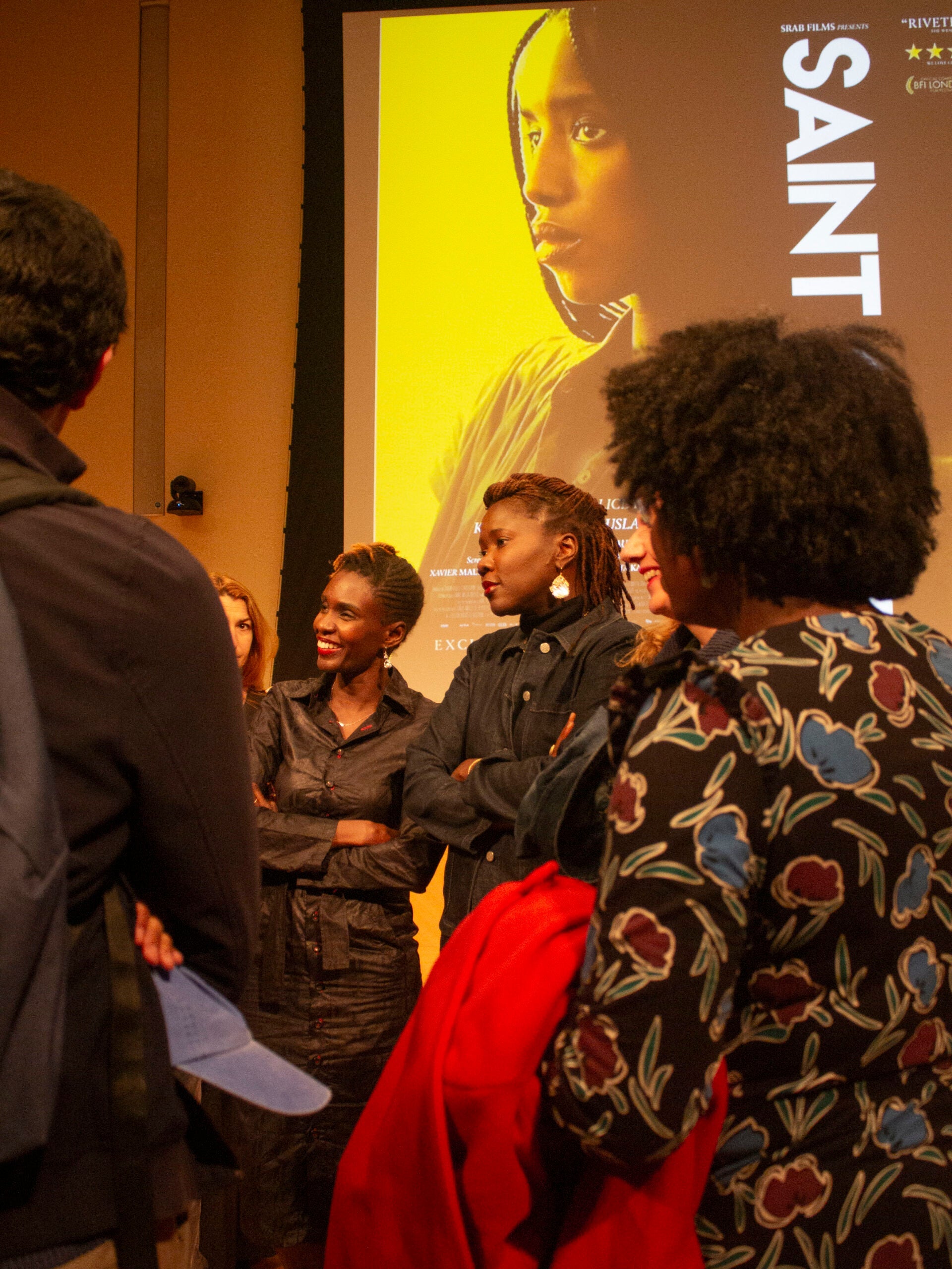 A group of women standing with their arms crossed in front of them, smiling and chatting with each other.