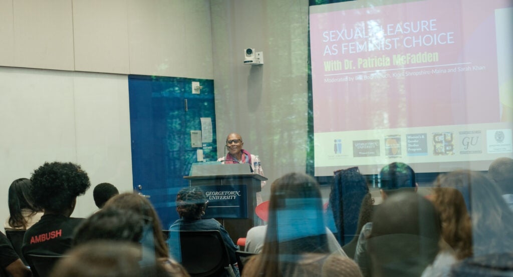 Dr. McFadden stands at a podium to lecture. Behind her is a screen titled, 'Sexual Pleasure a Feminist Choice.'