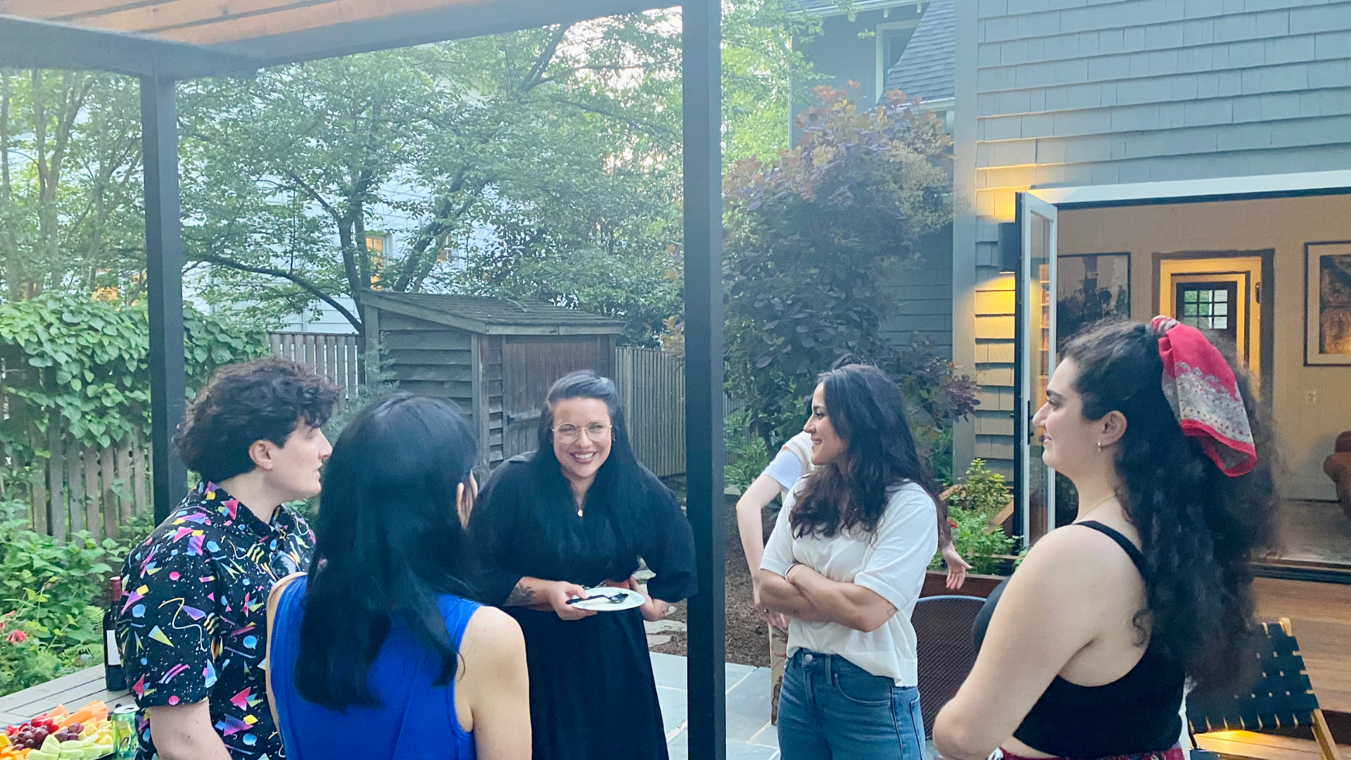 Five people standing in a circle in a backyard, chatting.