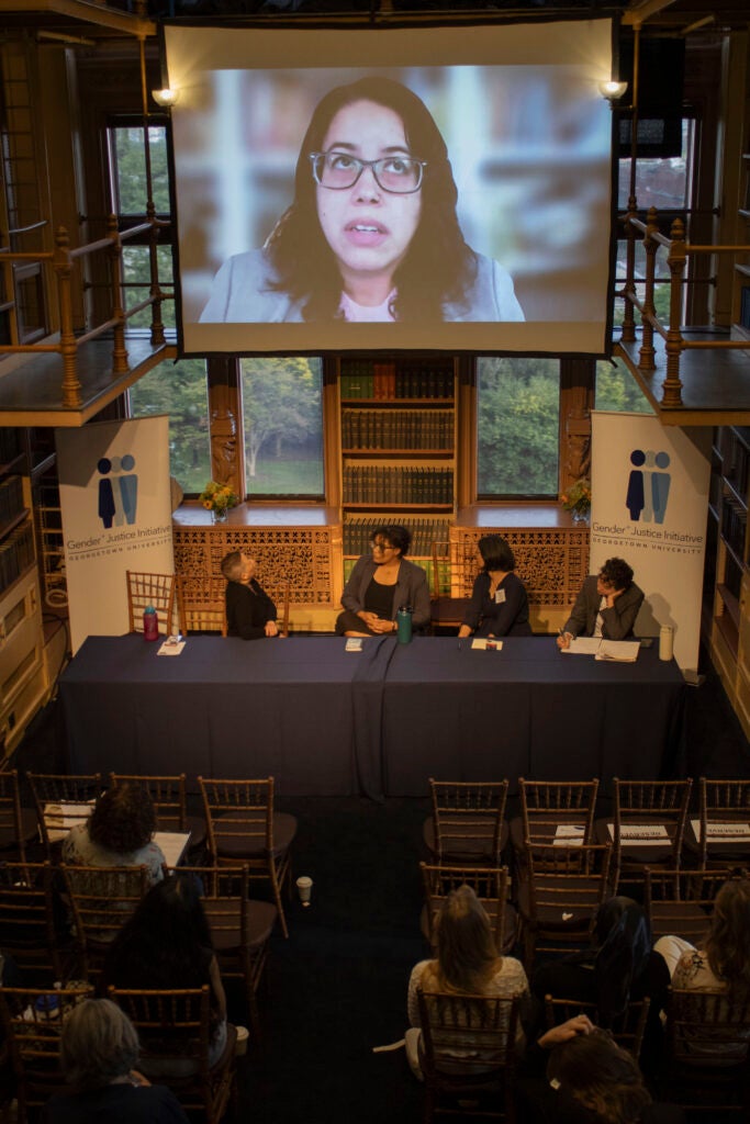 Four panelists from Panel 1, titled "Intersectional Approaches to Environmental and Social Justice," are seated at a rectangular table, while the fifth panelist joins virtually via Zoom. During the Q&A session, all panelists actively engage with the audience.