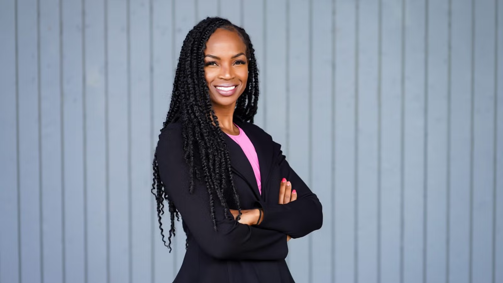 Jamillah Bowman Williams is smiling with her arms crossed. She is wearing a pink blouse beneath a navy blazer.