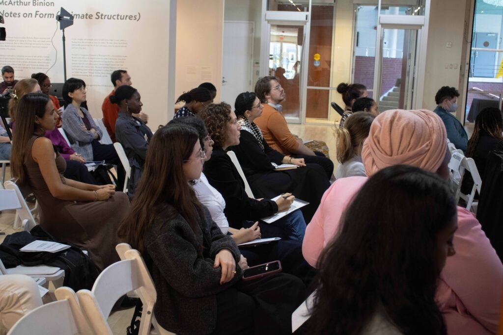 Audience members sit in rows, looking to the right.