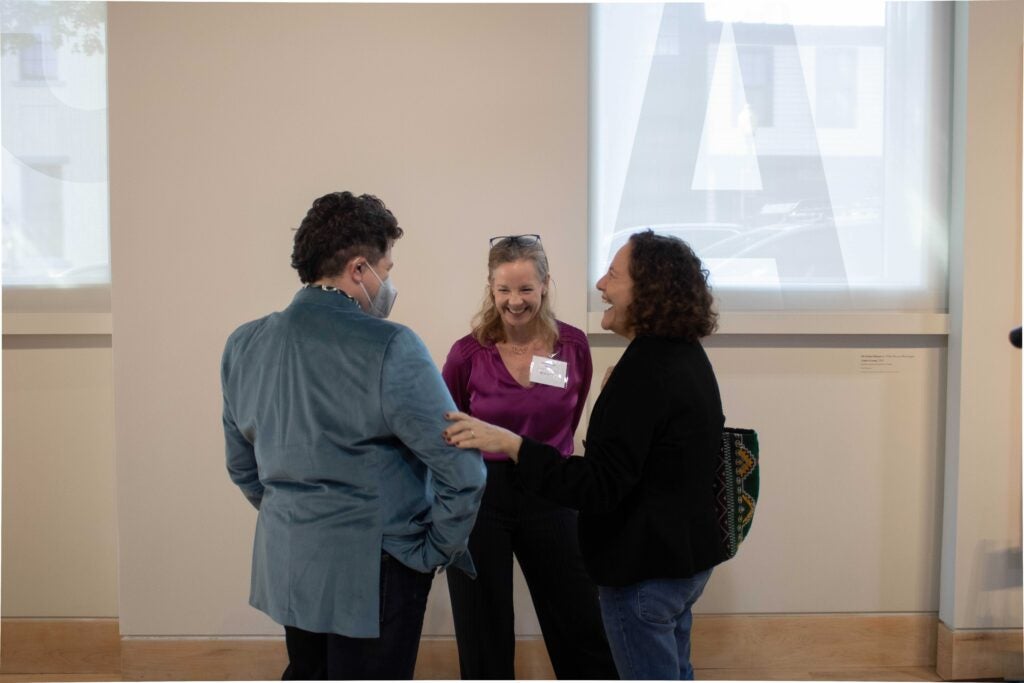Three people standing in a circle and laughing. The woman on the right laughs and places a hand on another person's elbow.
