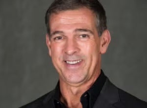 Headshot of Ricardo Ortiz, white man with salt and pepper short hair smiling wearing a black shirt and blazer.