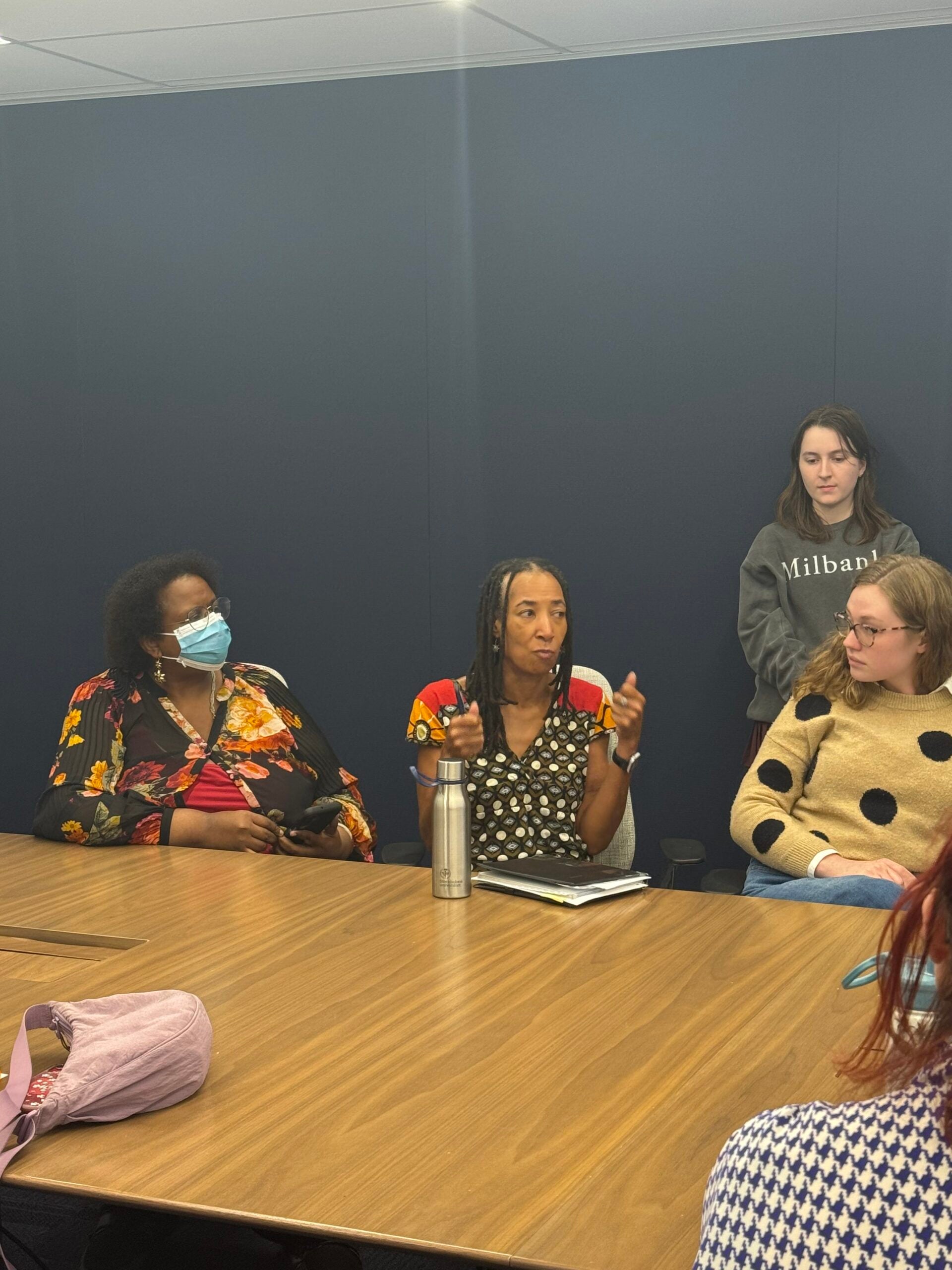 People sitting around a conference table. The woman in the middle is speaking.