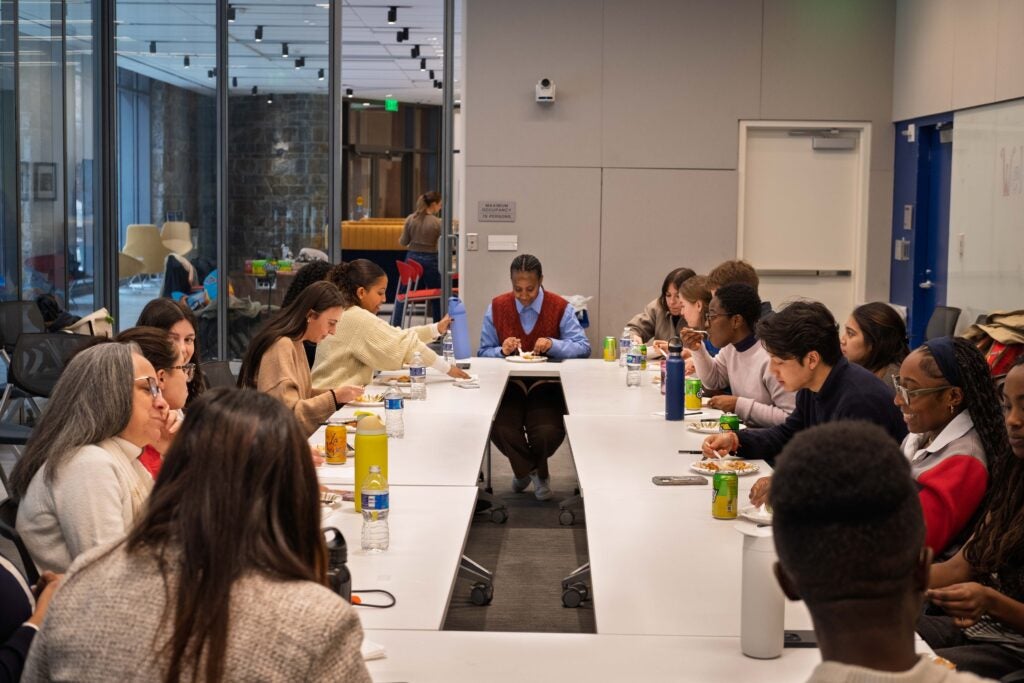 A large rectangular table of students and professors eating, smiling, and chatting with each other.