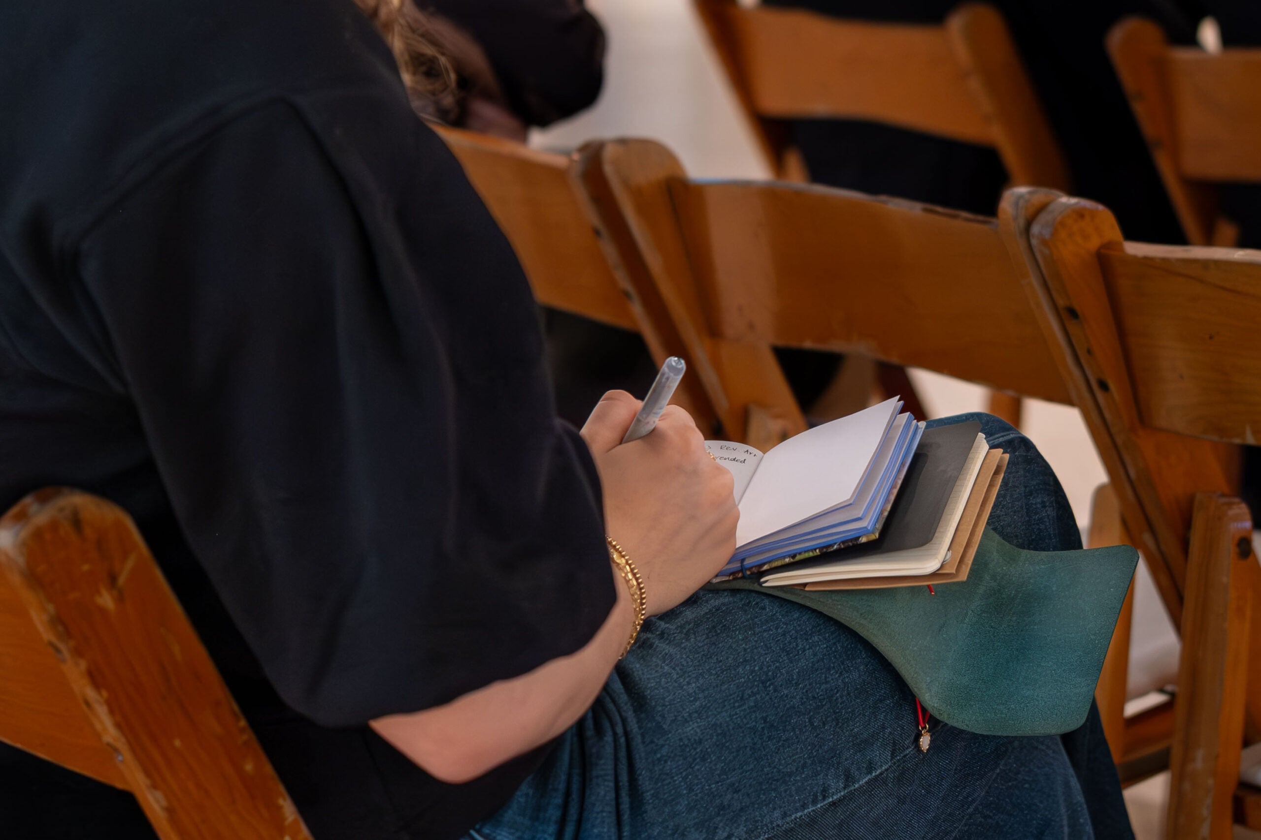 A woman writes notes into a small, leather-bound journal in her lap.
