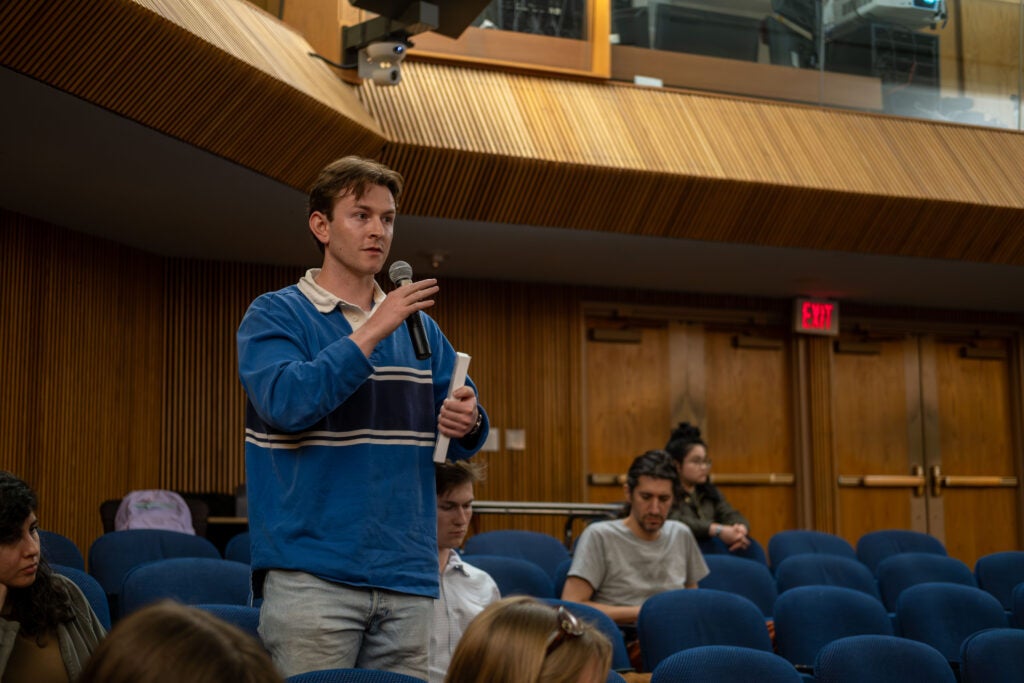 An audience member stands, holding a book under his arm and speaking into a microphone during the Q&A session.