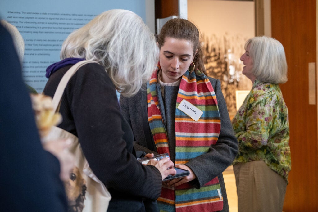 Two women looking down at one of their cell phones. The woman on the left is typing something on the phone, and the woman on the right looks down as she types.