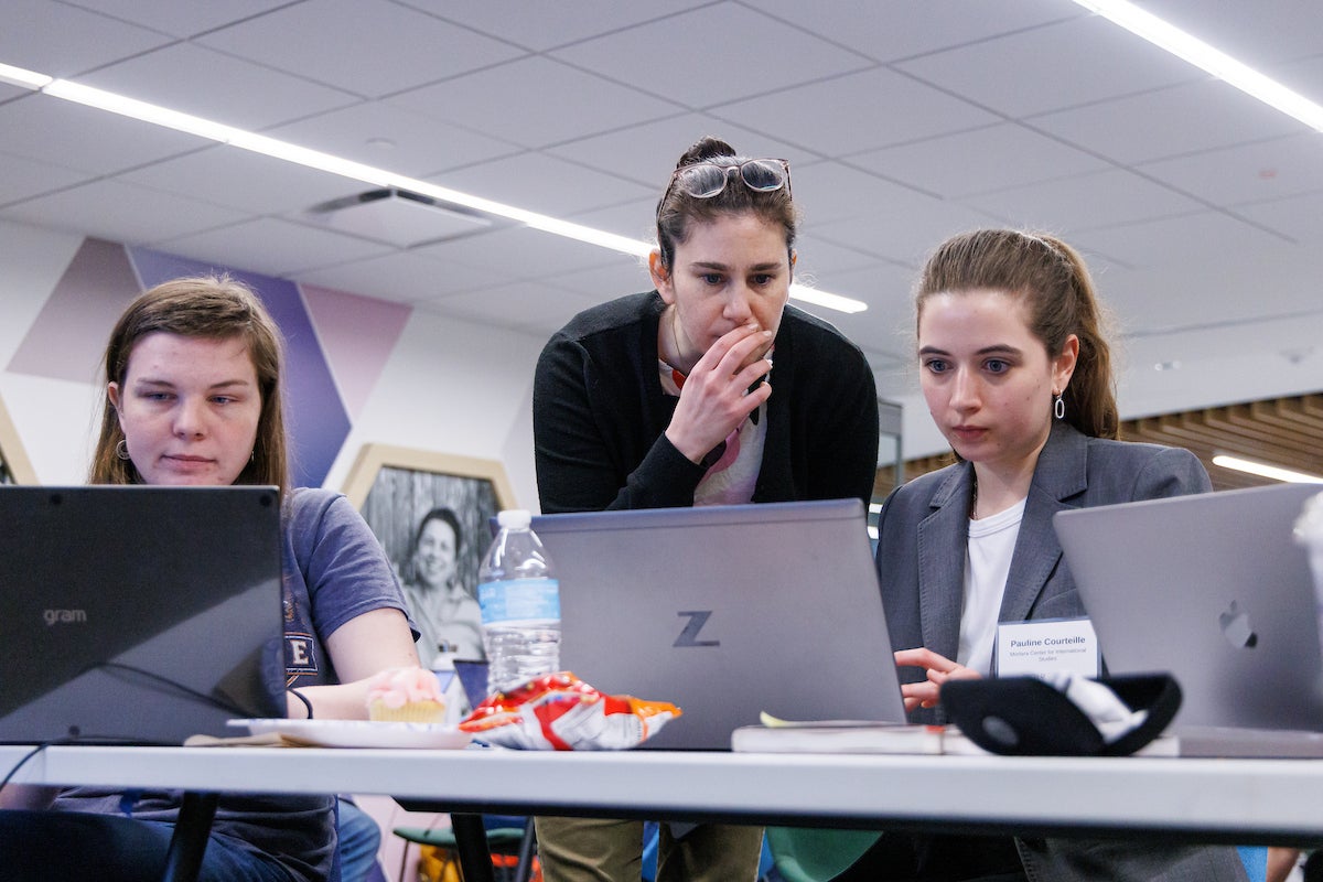 Three people sitting at a table, typing on laptops.