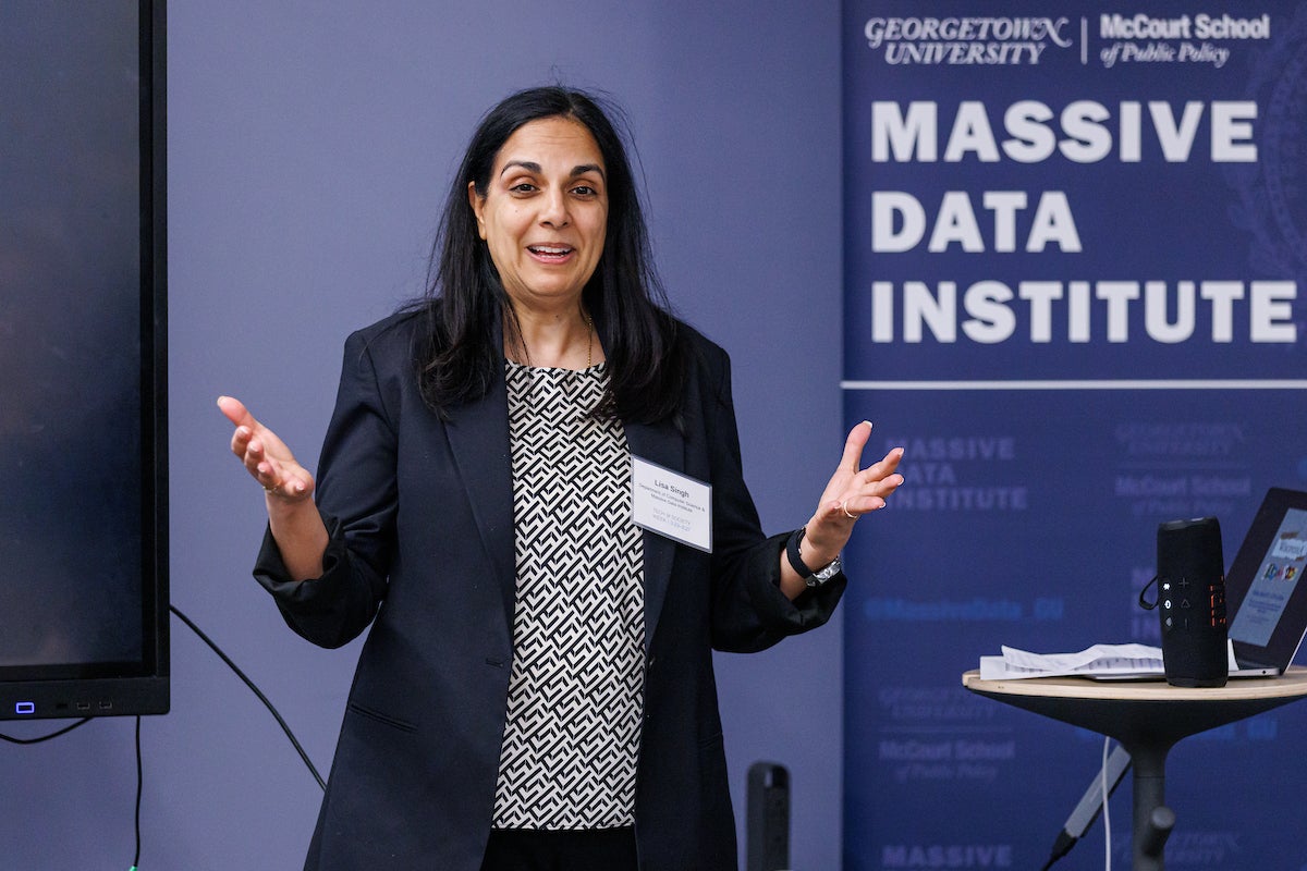A woman wearing a name tag standing behind a podium, talking.