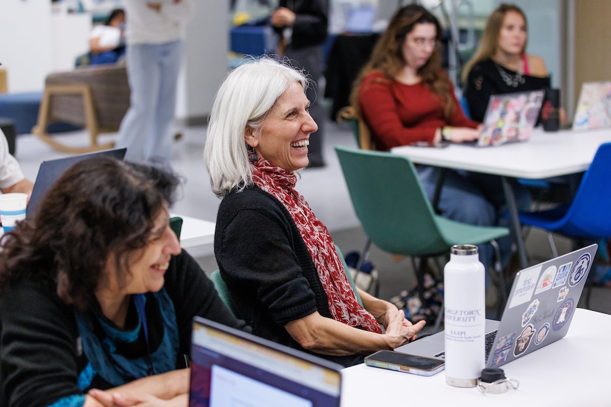 Several women seated at tables with laptop computers, laughing.