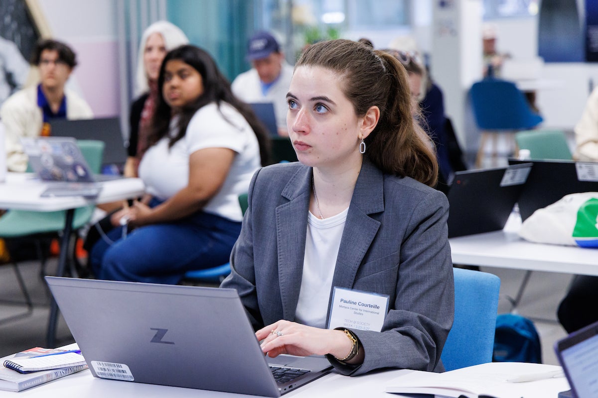 A woman sitting at a table, wearing a nametag. She is typing on a laptop computer.