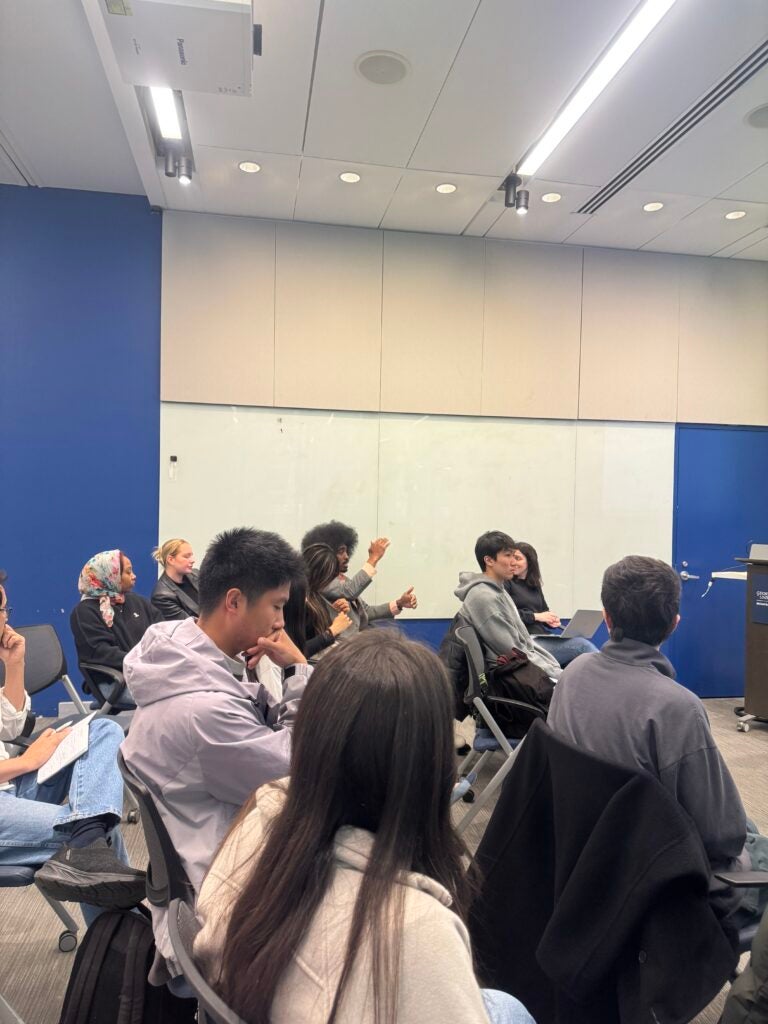 A group of seated audience members. One person in the back is speaking and gesturing with his hands.